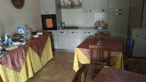 Une cuisine compacte avec des meubles blancs, une cuisinière à gaz et un évier. On y trouve deux tables à manger, recouvertes de nappes rouges et jaunes, ainsi que des chaises disposées autour.