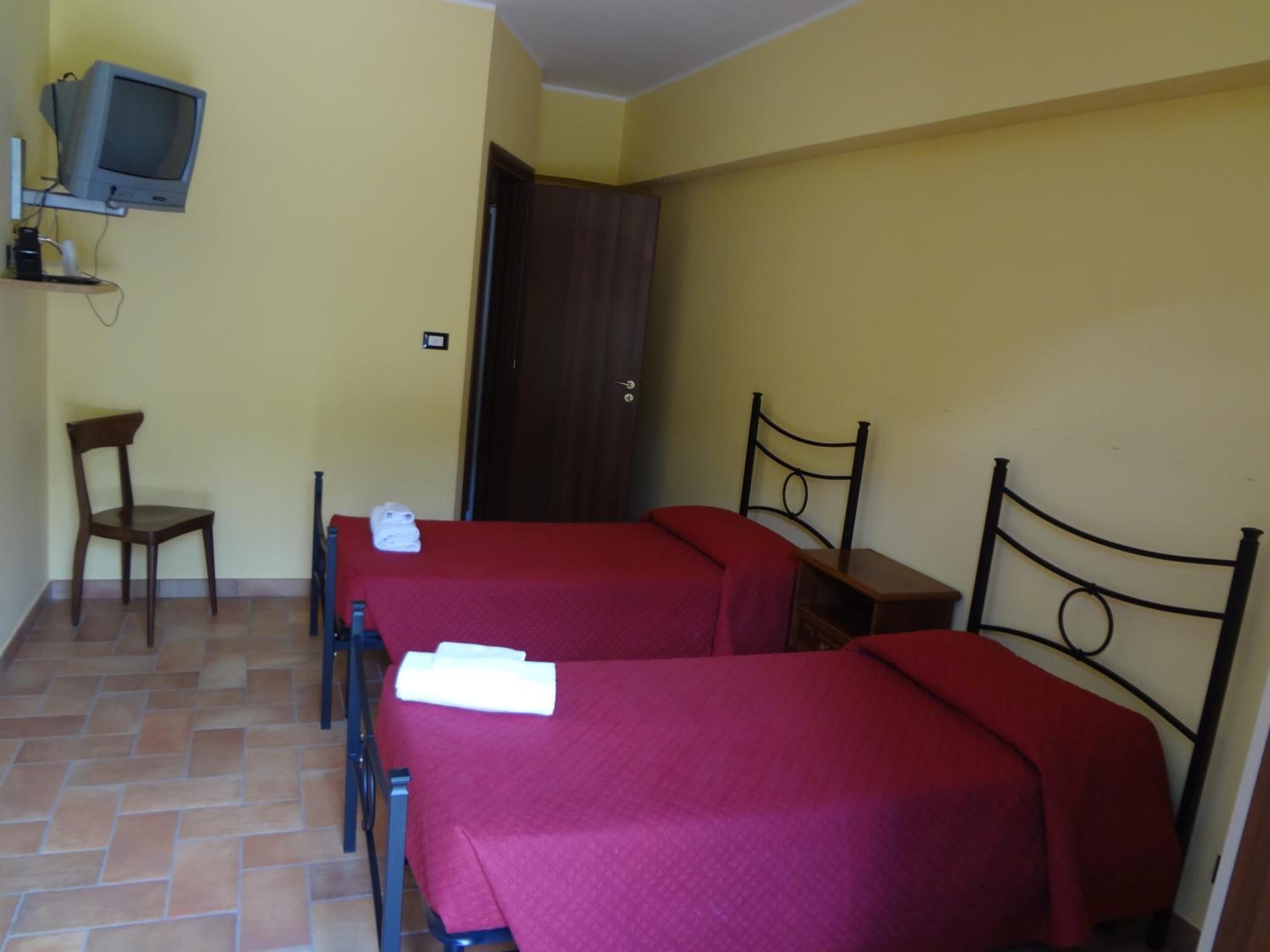 A room with two beds, a chair, a television, and a door.