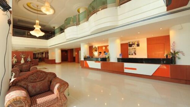 Een ruime lobby met een receptiebalie, een hoog plafond met kroonluchters en een zithoek met een gestreept banksofa.