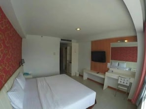 Et hotelværelse med seng, skrivebord, stol, fjernsyn og spejl.