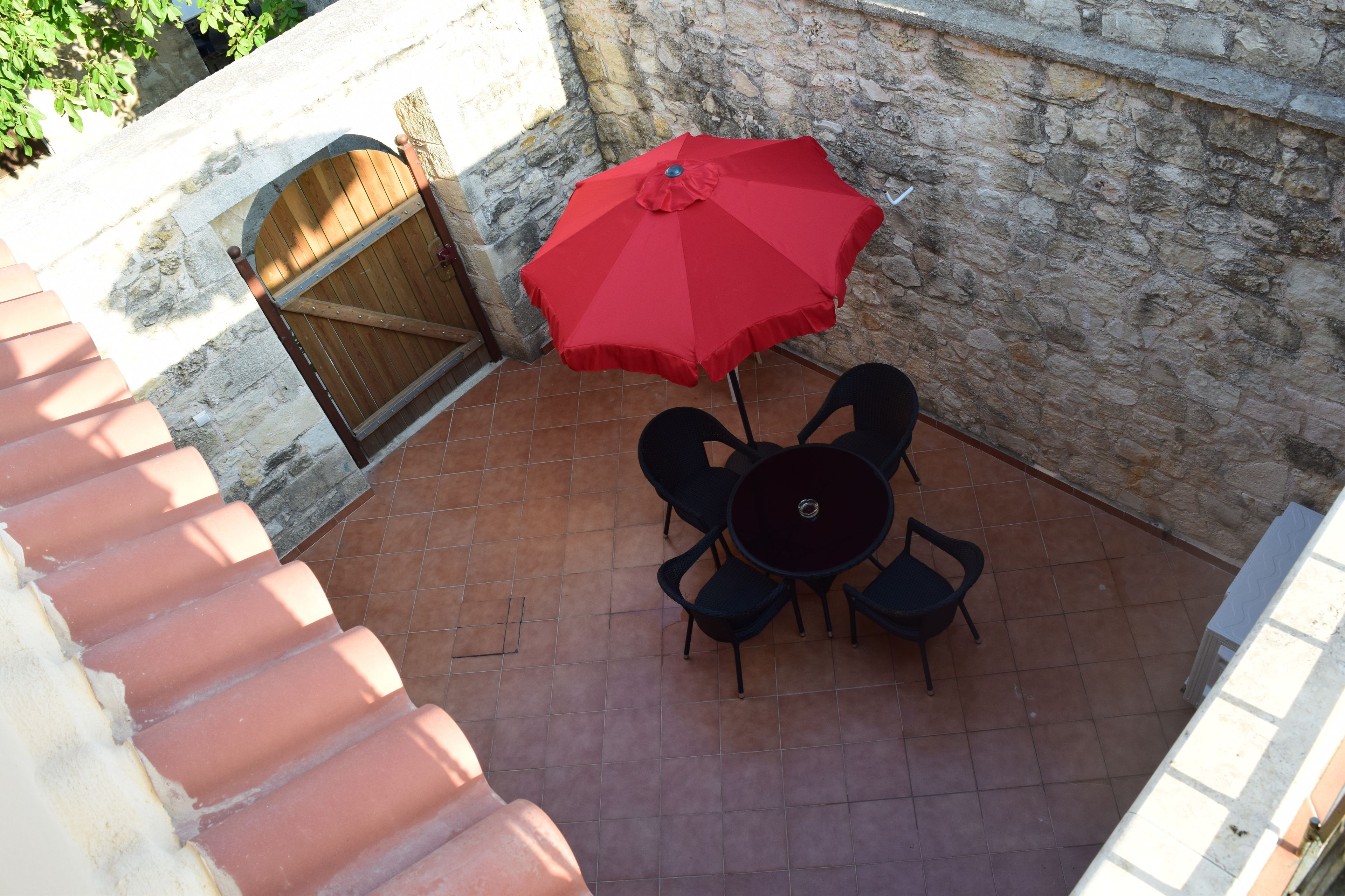A patio with a red umbrella, a round table, and four chairs.