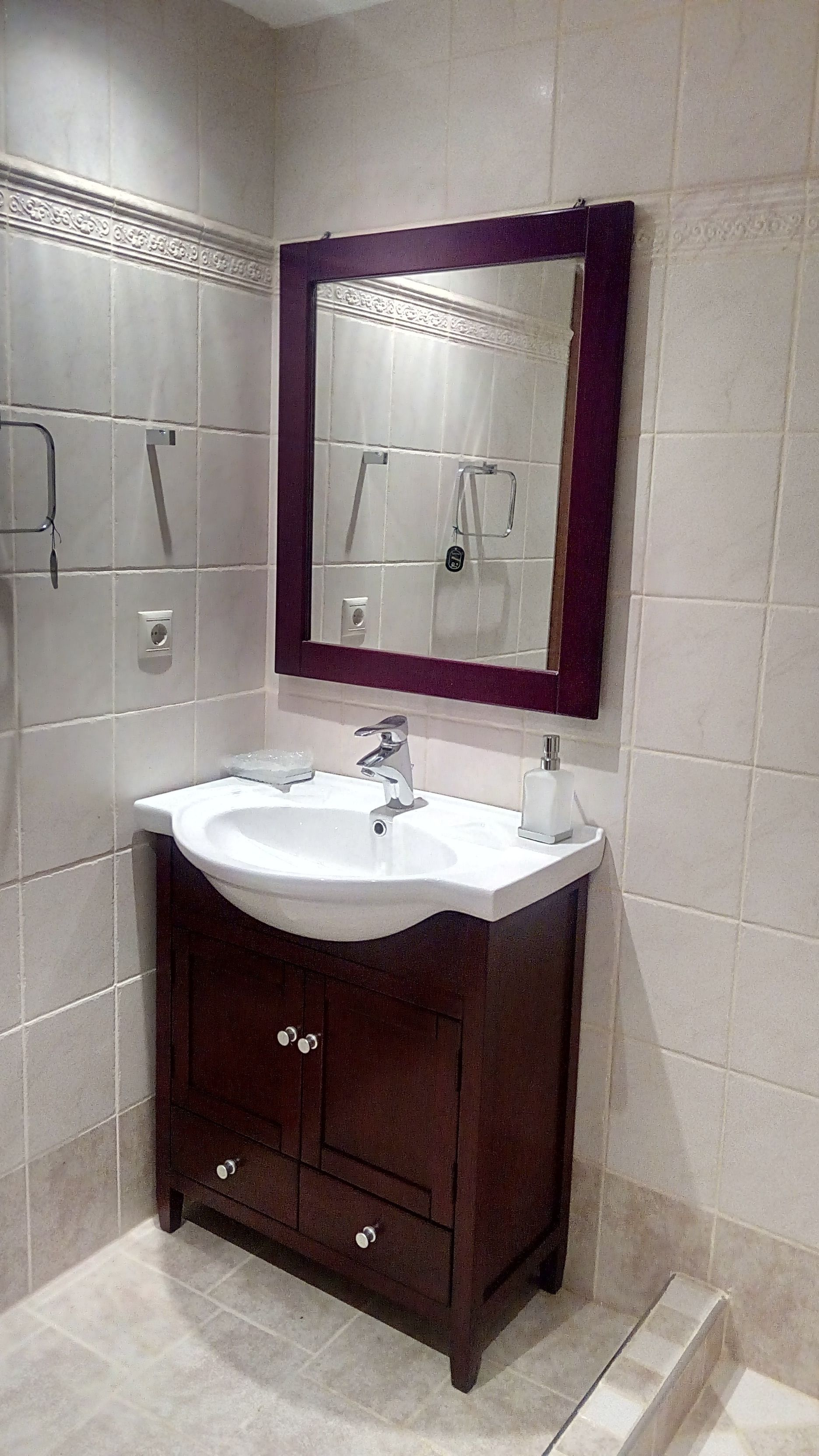 Un baño con lavamanos blanco, tocador de madera oscura y espejo con marco morado.