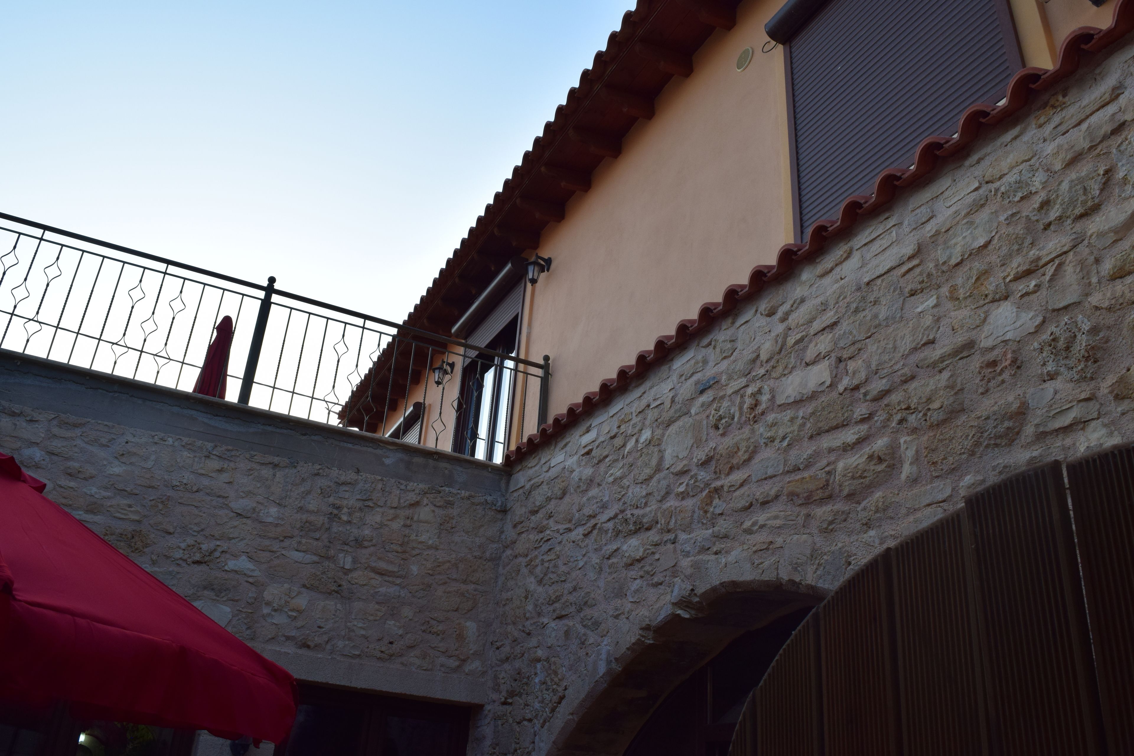 A stone building with a balcony and a red umbrella.