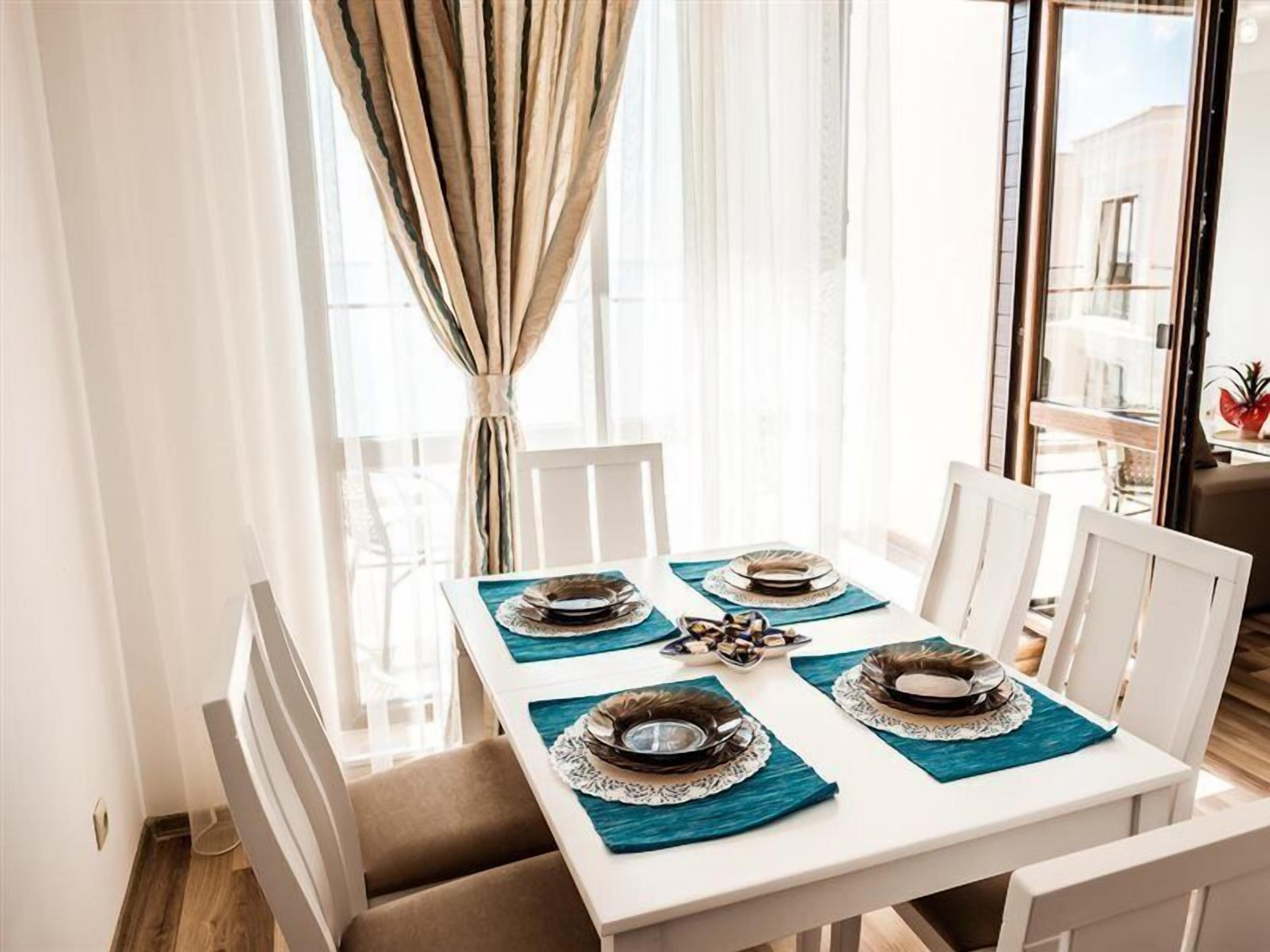 A dining area with a white table set for four, featuring teal placemats and silverware.
