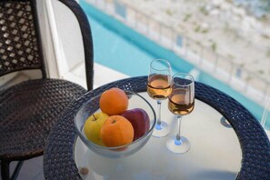 A glass bowl with fruits and two wine glasses on a table by a pool.