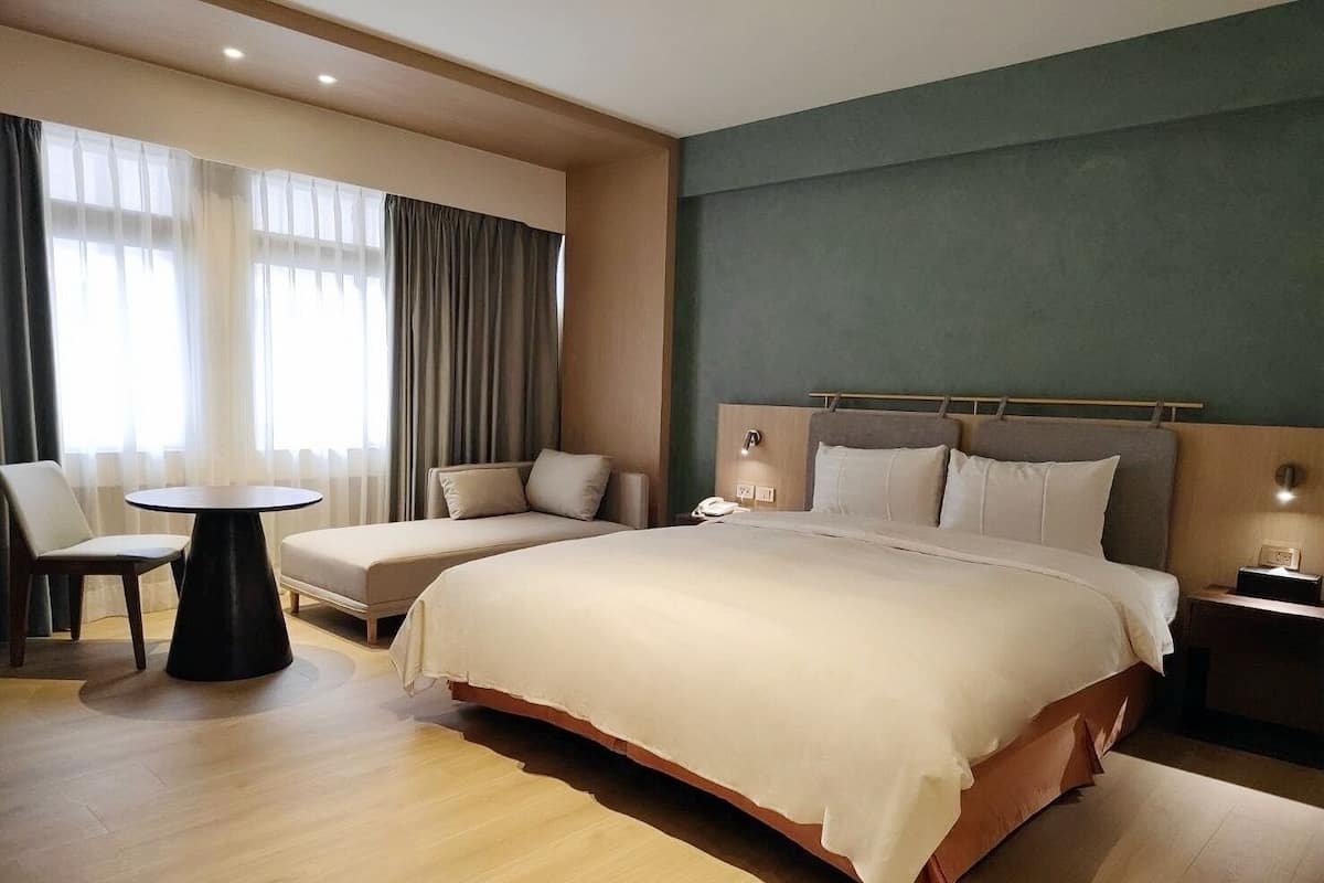 Quarto de hotel com uma cama grande, uma cama menor, uma mesa redonda e uma cadeira.