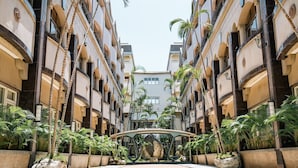 Un hotel a più piani con balconi, palme e un arco centrale.