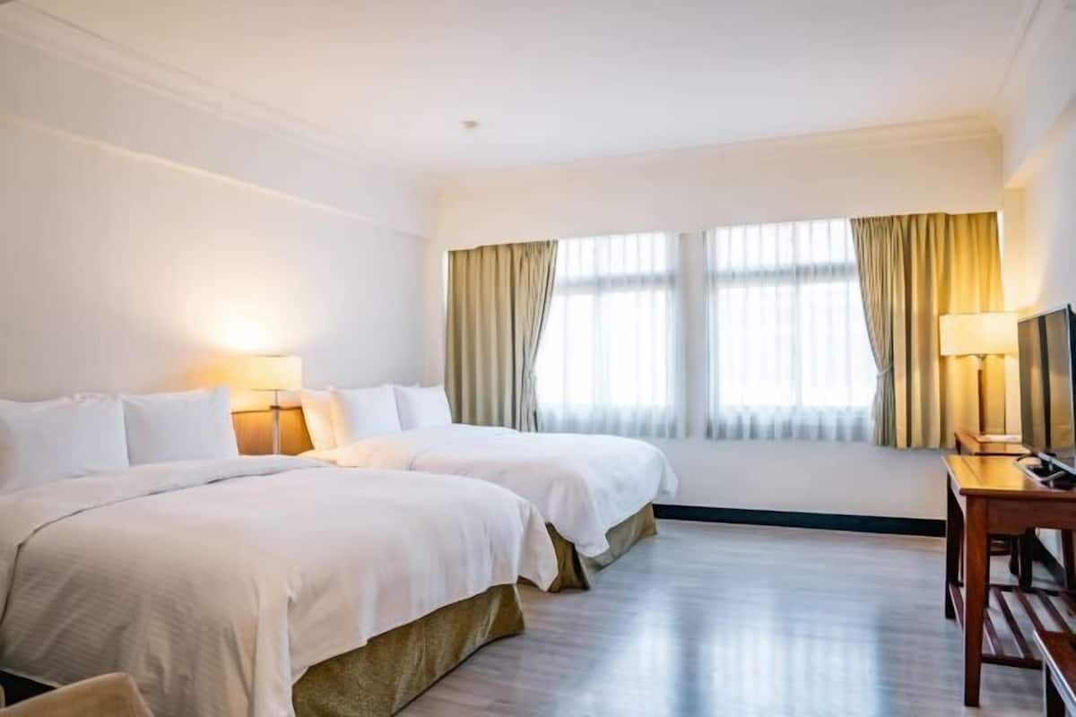 Quarto de hotel com duas camas, uma escrivaninha e uma janela grande com cortinas.