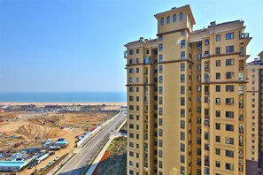 A high-rise building with multiple balconies, a view of the beach, and construction activity in the foreground. - Blessed Family Seaview Apartment 1601 (Qingdao)