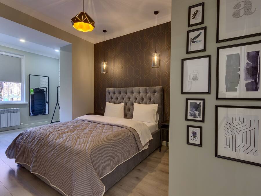 A bedroom with a tufted headboard, a large bed with a striped bedspread, two pendant lights, and framed artwork on the wall.