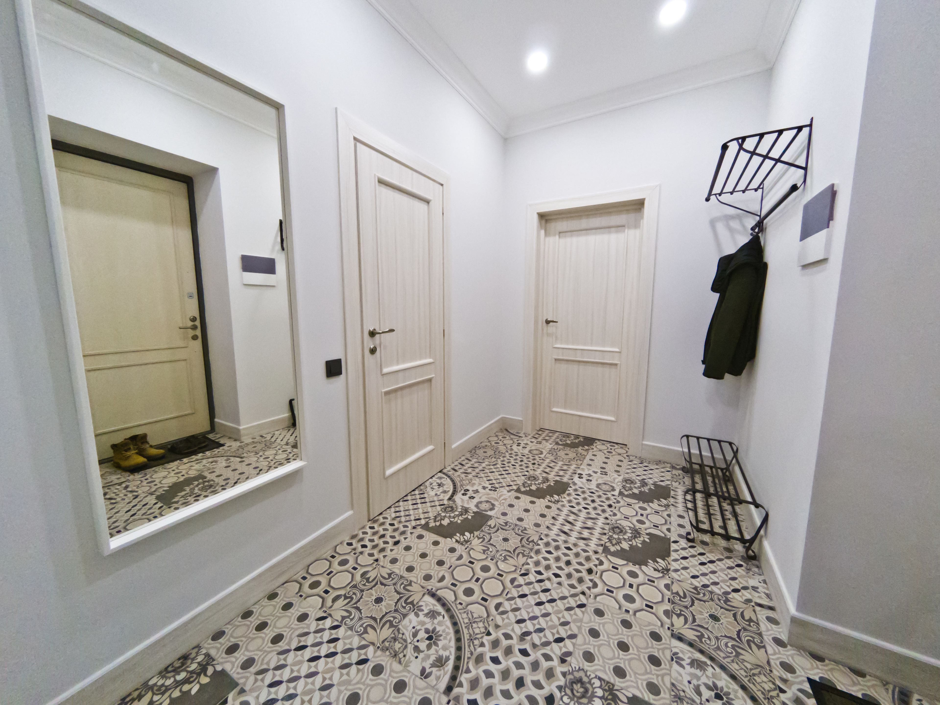 Un couloir avec des carreaux de sol à motifs, des portes blanches et un porte-manteau sur lequel est accrochée une veste.