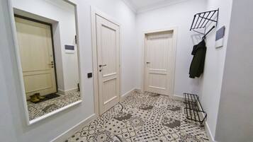 Un couloir avec des carreaux de sol à motifs, des portes blanches et un porte-manteau sur lequel est accrochée une veste.