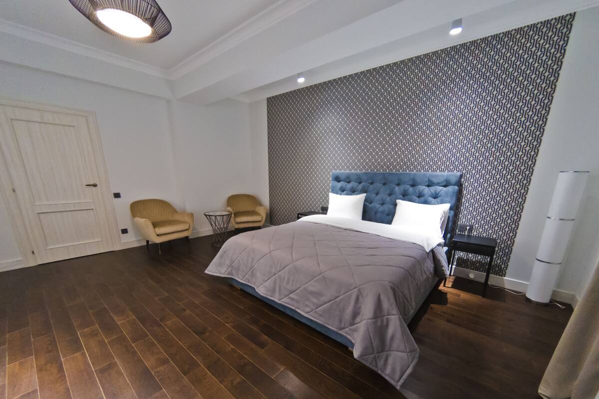Un dormitorio moderno con una cama grande, dos sillones, una mesita y un papel tapiz estampado.
