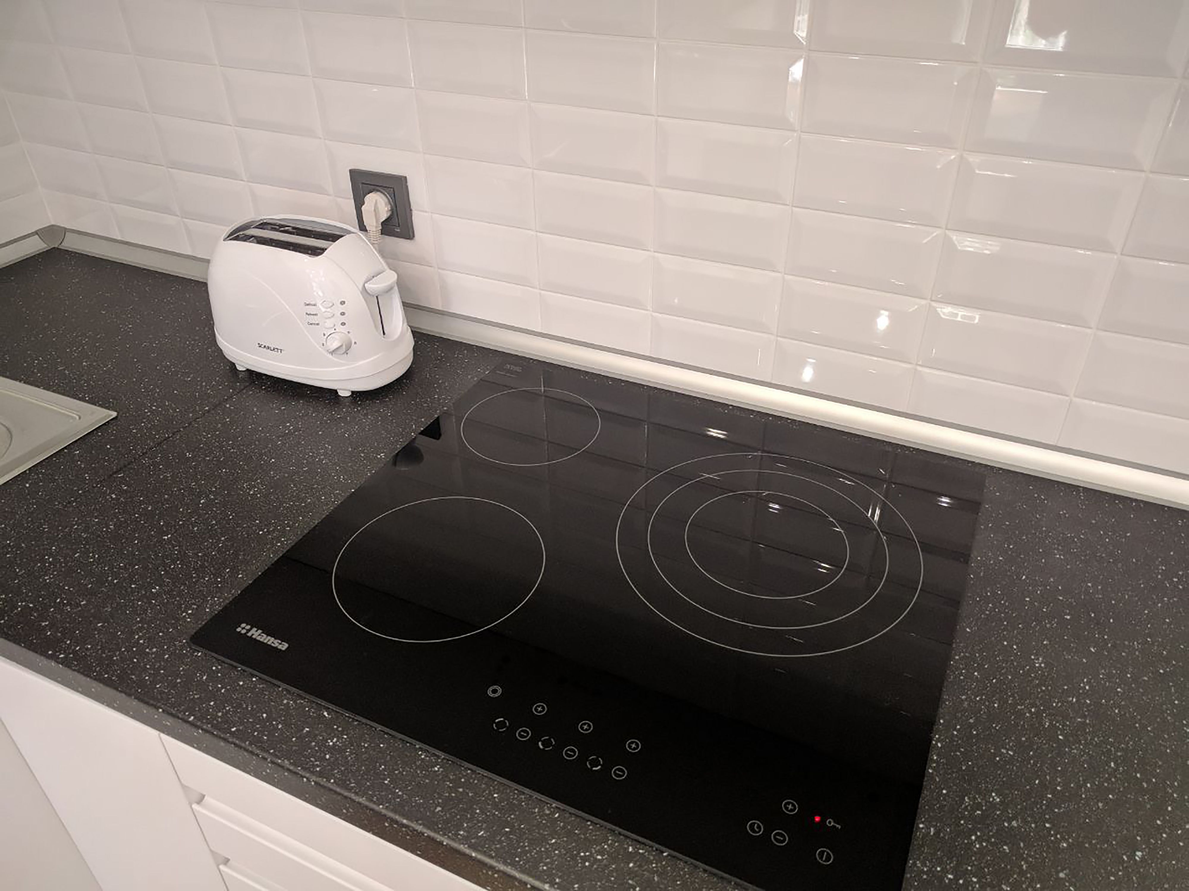 Cozinha com um fogão por indução preto e uma torradeira branca.