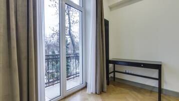 A room with a large sliding glass door leading to a balcony, a black desk with drawers, and a wooden floor.