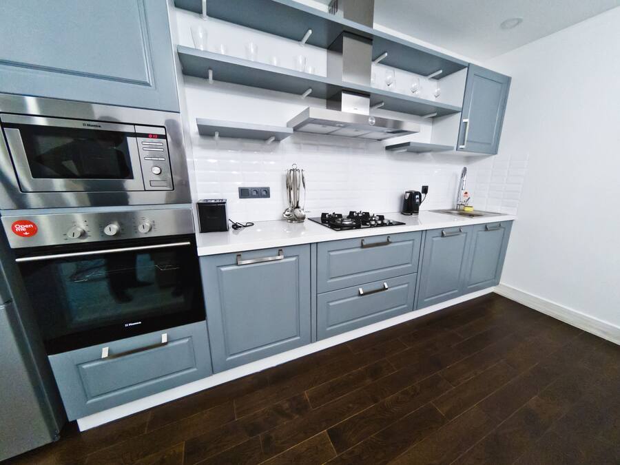 Une cuisine moderne avec des meubles gris, un plan de travail blanc, des appareils en acier inoxydable et un parquet en bois foncé.