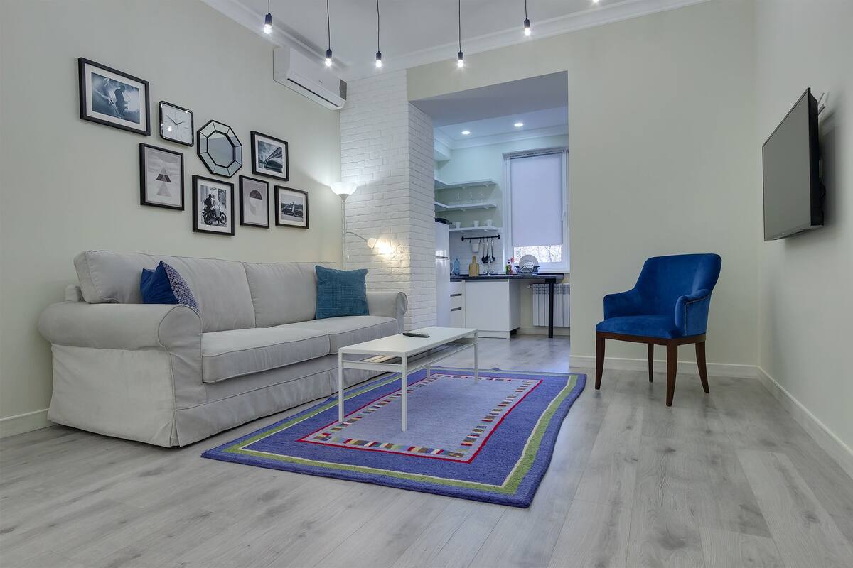 Una sala de estar con un sofá blanco, un sillón azul, una mesa de centro y una alfombra estampada.