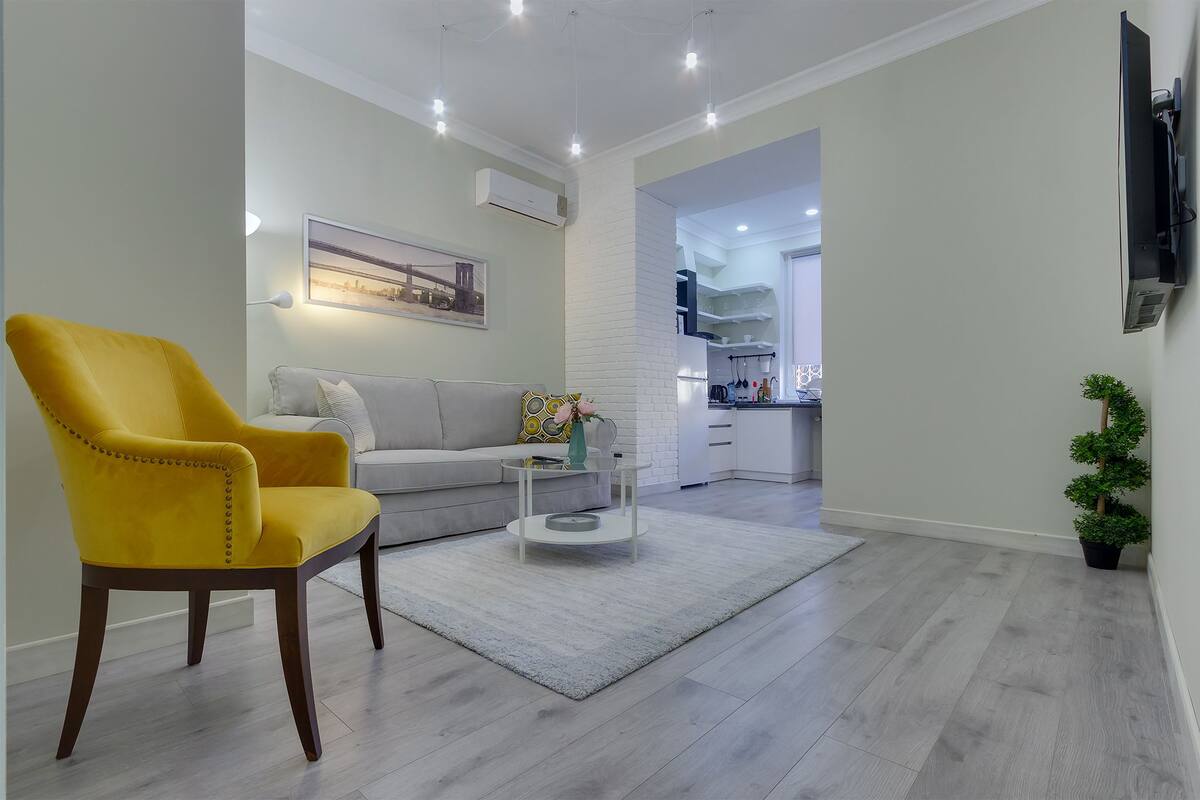 Una sala de estar moderna con un sillón amarillo, un sofá gris, una mesita de centro de cristal y una pequeña planta en maceta.