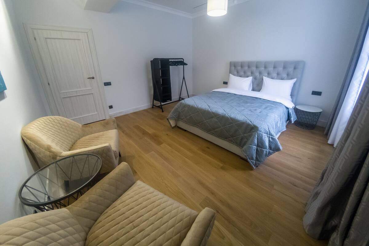 Un dormitorio con cama, dos sillas, una mesita, un armario y una lámpara colgante.