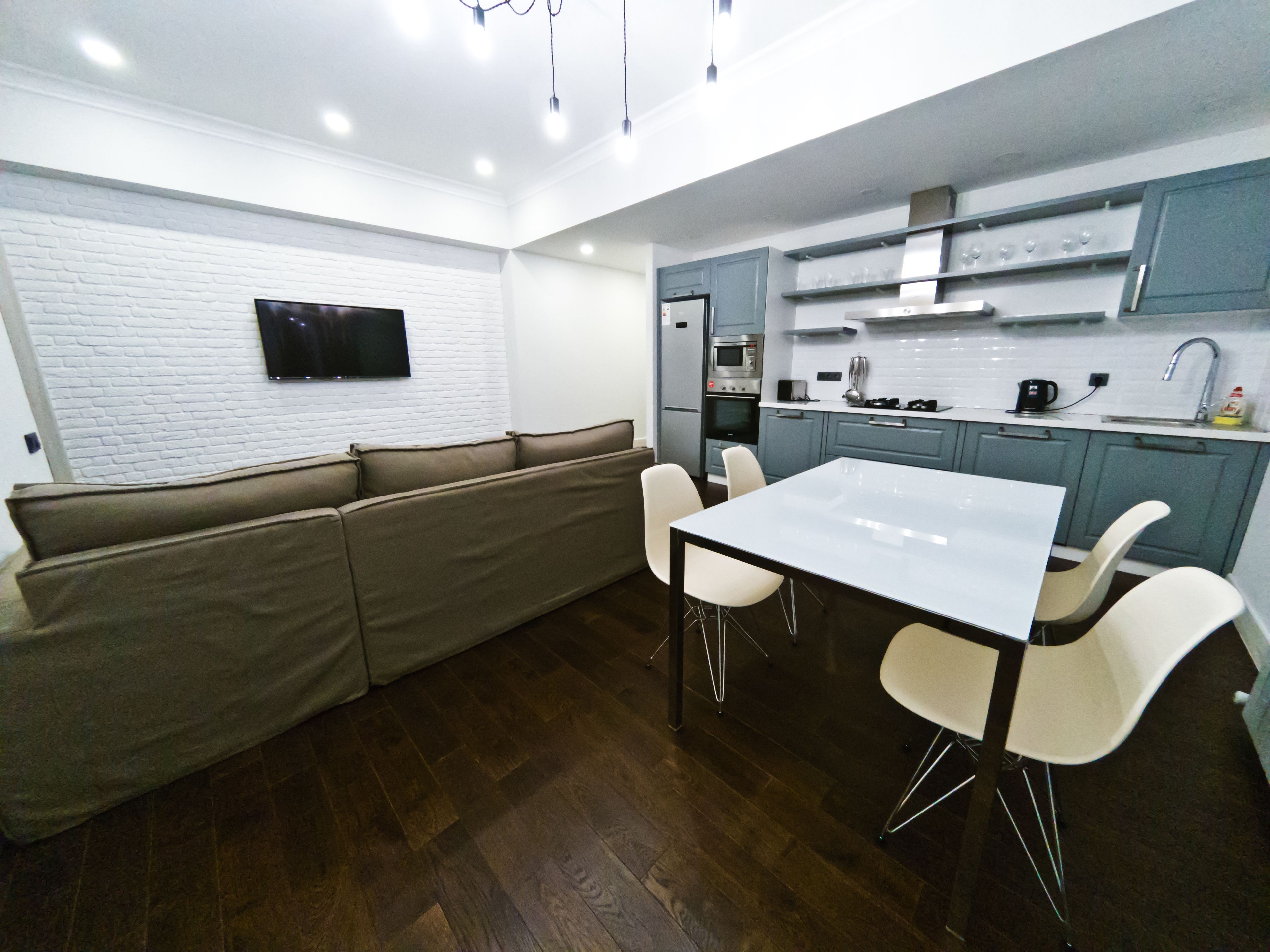 A modern kitchen with a built-in oven, microwave, and sink. There is a white dining table with four chairs and a beige sofa.