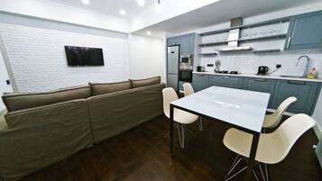 A modern kitchen with a built-in oven, microwave, and sink. There is a white dining table with four chairs and a beige sofa.