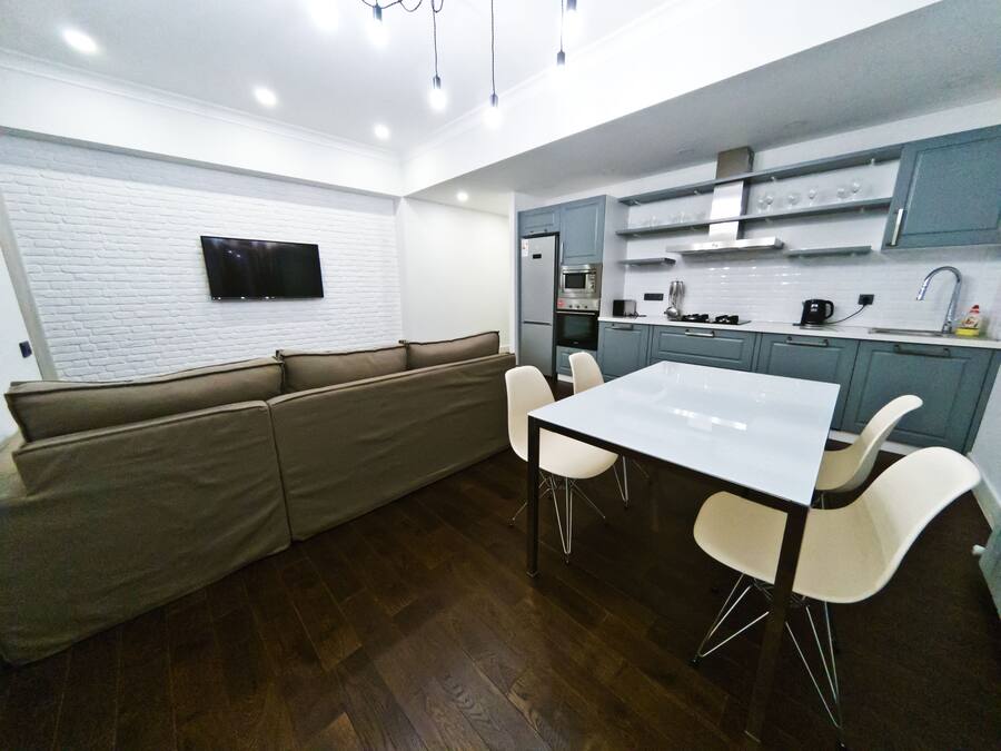 A modern kitchen with a built-in oven, microwave, and sink. There is a white dining table with four chairs and a beige sofa.