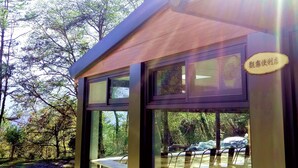 A modern outdoor seating area with glass walls, a wooden table, and chairs. - Guanwu Villa (Taian)