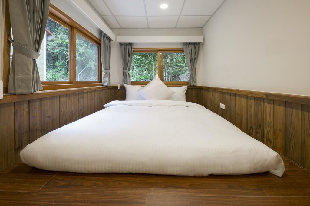 A large bed in a room with wooden paneling and a view of greenery through the windows.
