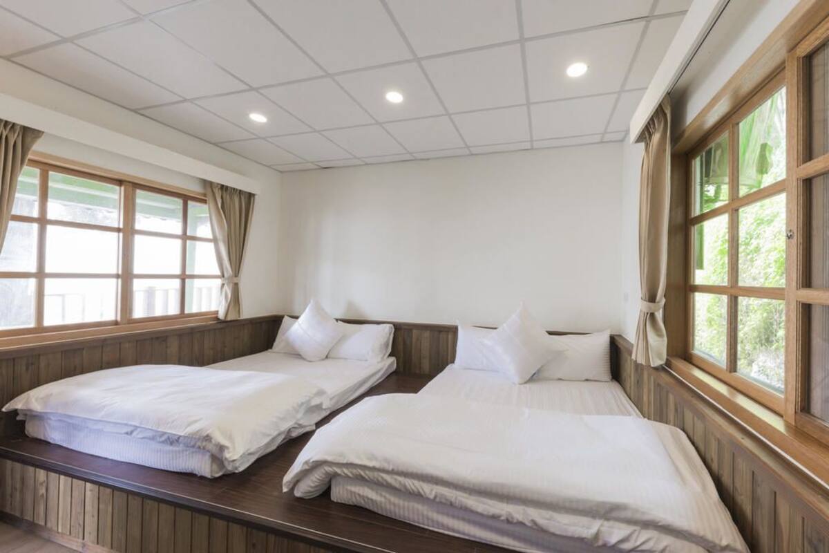 A hotel room with two single beds, wooden paneling, large windows with curtains, and a tiled ceiling.