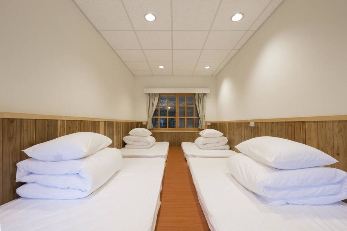 A hotel room with two single beds, a wooden headboard, a window with curtains, and a tiled ceiling.