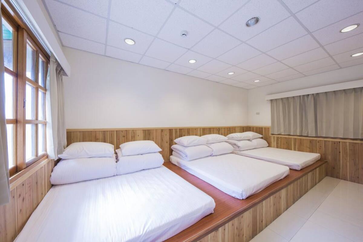 A hotel room with three single beds, wooden headboards, and a large window with curtains.