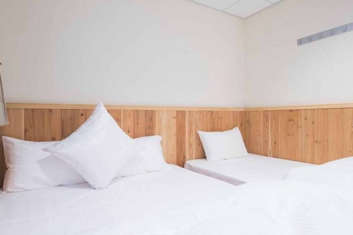 Una habitación con dos camas, cabecera de madera, ropa de cama blanca y pared de color claro.