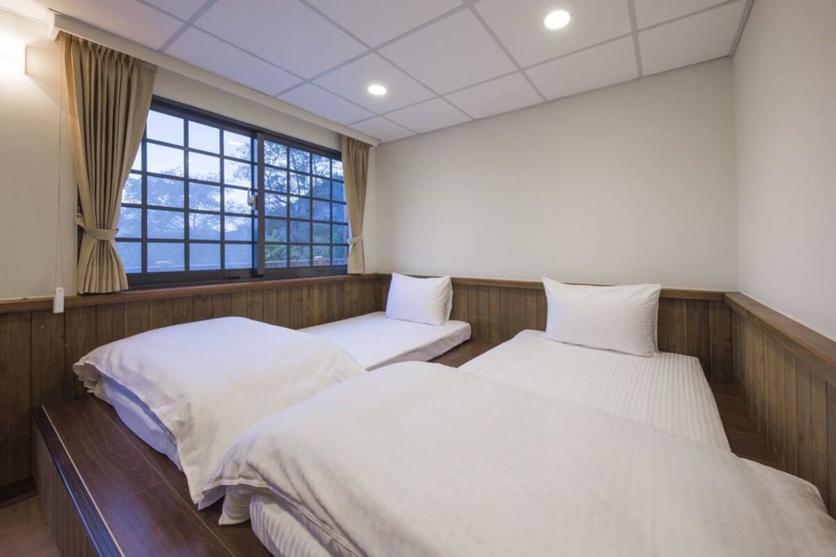 A hotel room with two beds, wooden paneling, a large window with curtains, and a tiled ceiling.