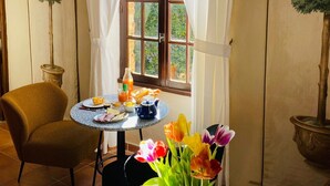 A dining area with a table set for breakfast, a chair, a vase of flowers, and a window with curtains. - La Vieille Demeure (Torreilles)