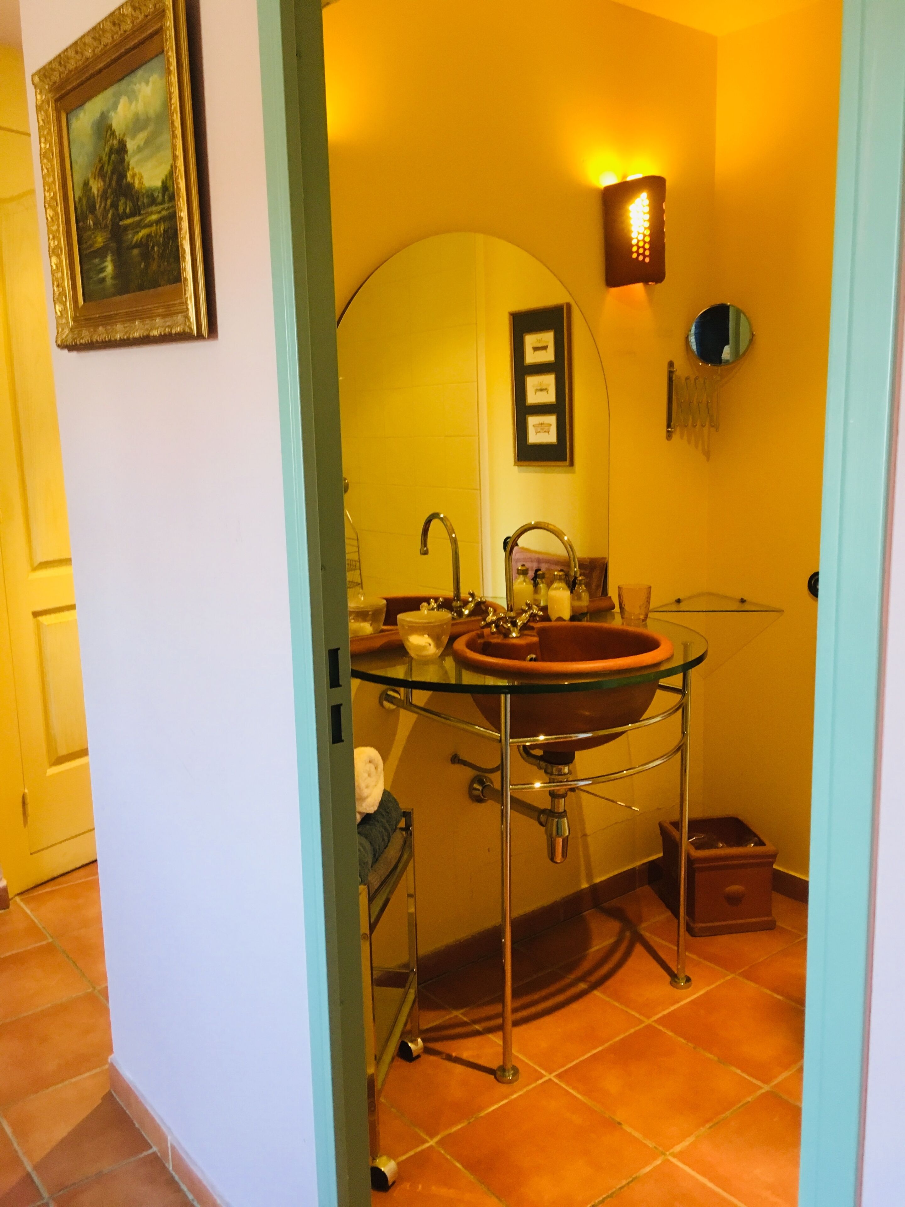 A bathroom with a glass sink, a mirror, and a wall-mounted light fixture.