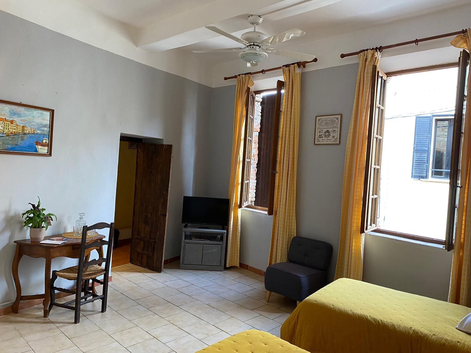 Une pièce comprenant un lit, un bureau, une chaise, un téléviseur et un ventilateur de plafond.