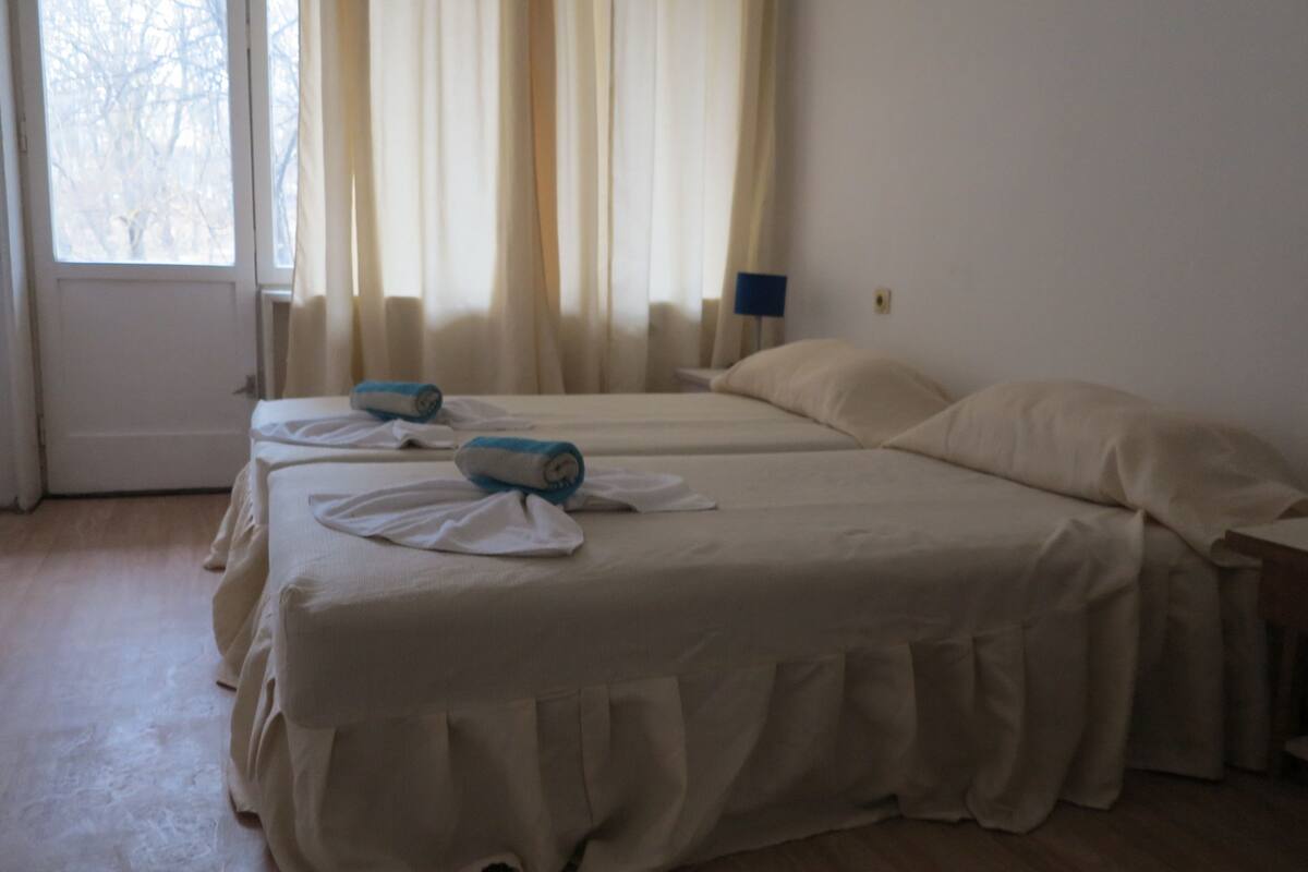 A hotel room with two beds, a window with curtains, and a bedside lamp.