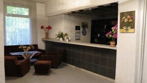 A room with a dining table, chairs, a small sofa, and a fireplace. There are flower arrangements on the mantel and a window with a view of trees. - Tango (Golden Sands)