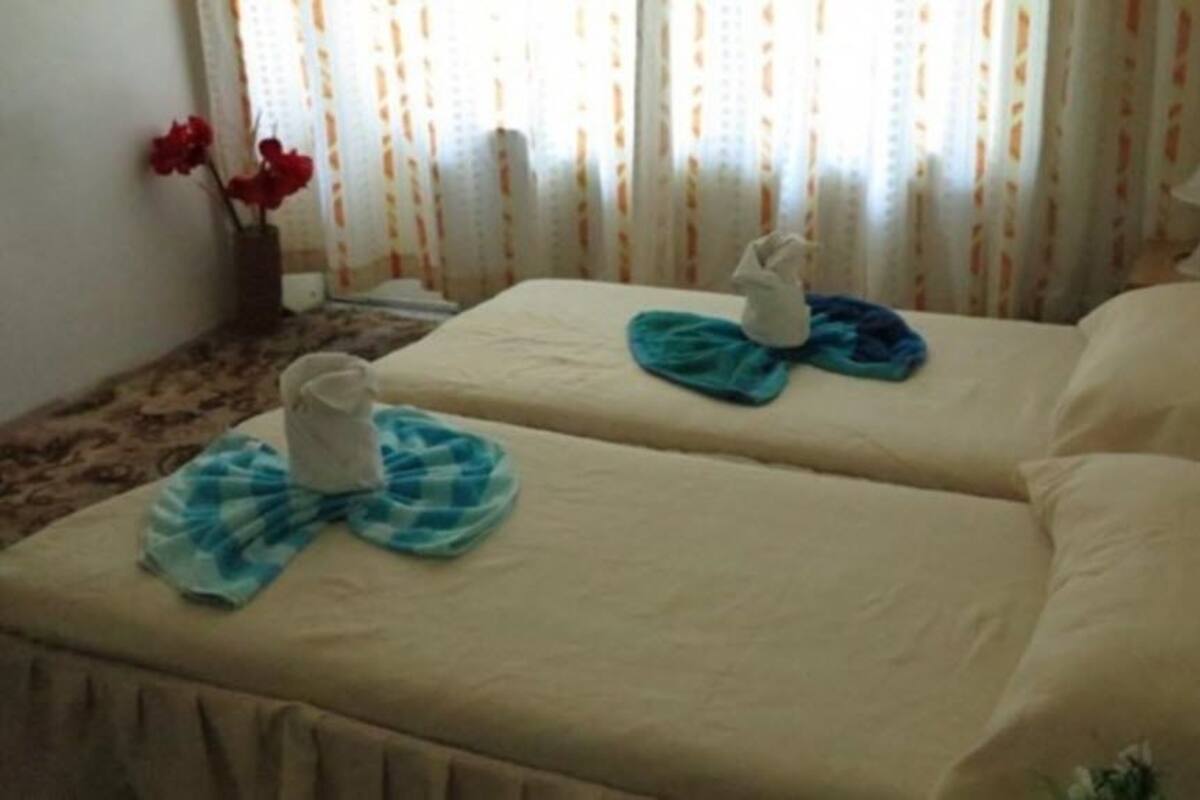 A hotel room with two beds, each with a towel and a small table.