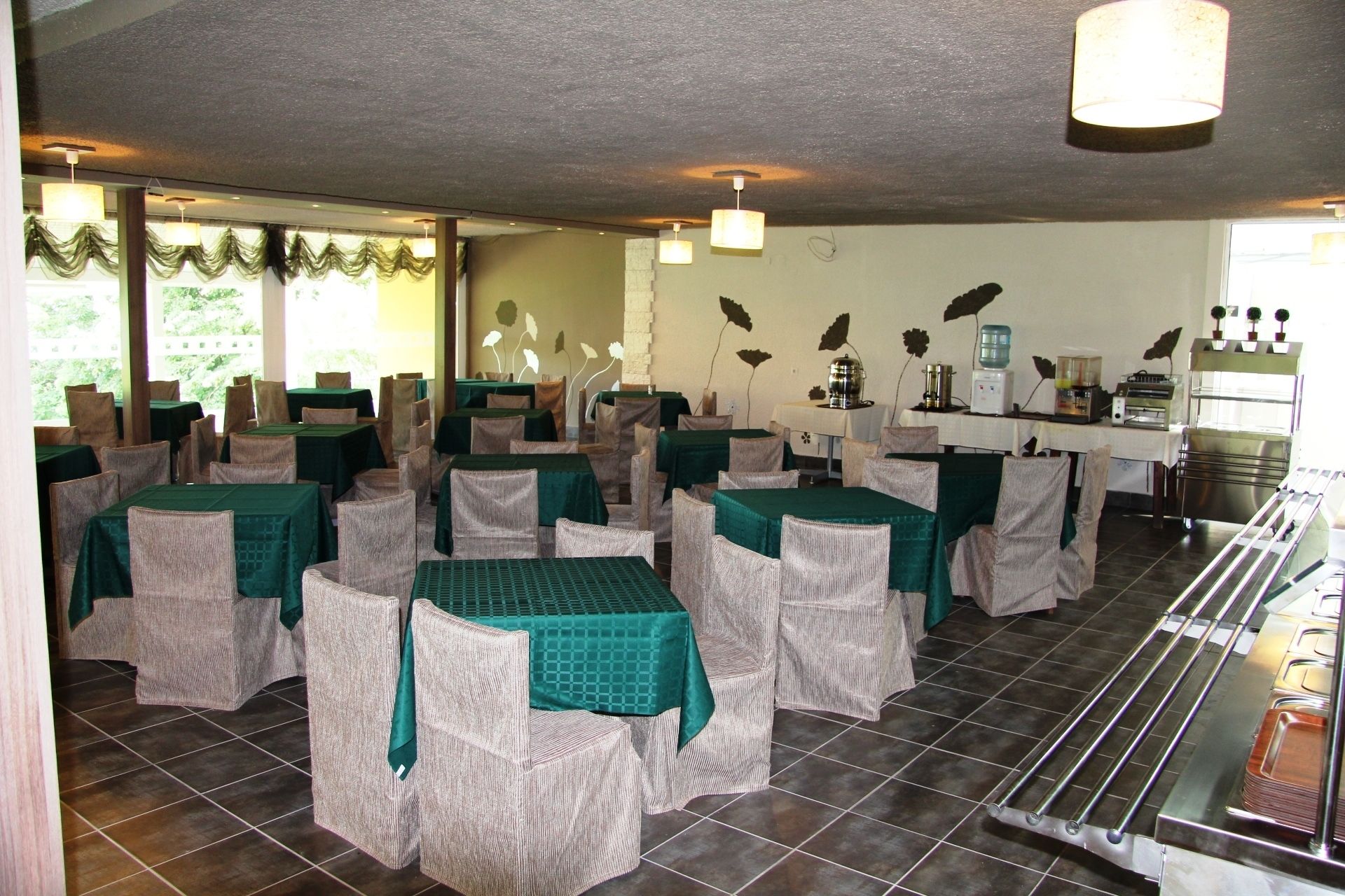 A dining area with tables and chairs, a kitchen area with appliances, and a view of greenery outside.