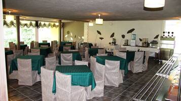 A dining area with tables and chairs, a kitchen area with appliances, and a view of greenery outside.