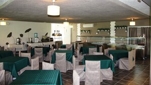 A restaurant with tables covered in green tablecloths and wicker chairs, a buffet area with a glass display, and a kitchen in the background. - Hotel Zarya- All Inclusive Light (Golden Sands)