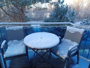 An outdoor patio with a round table and chairs covered in snow, surrounded by a glass enclosure with snow on the edges.