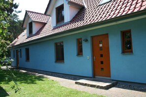 A single-story building with a red-tiled roof, a blue exterior, and a wooden door.