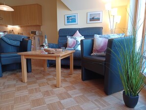 A cozy living room with a wooden table, two sofas, a potted plant, and a kitchen in the background. - Beach house Jonathan 4 OG (Wustrow)