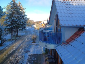 A snowy residential area with a house featuring a balcony and a tiled roof.