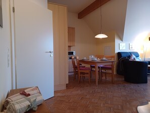 Et værelse med et spisebord dækket til fire personer, trægulv, en sofa og et tekøkken med en mikrobølgeovn.