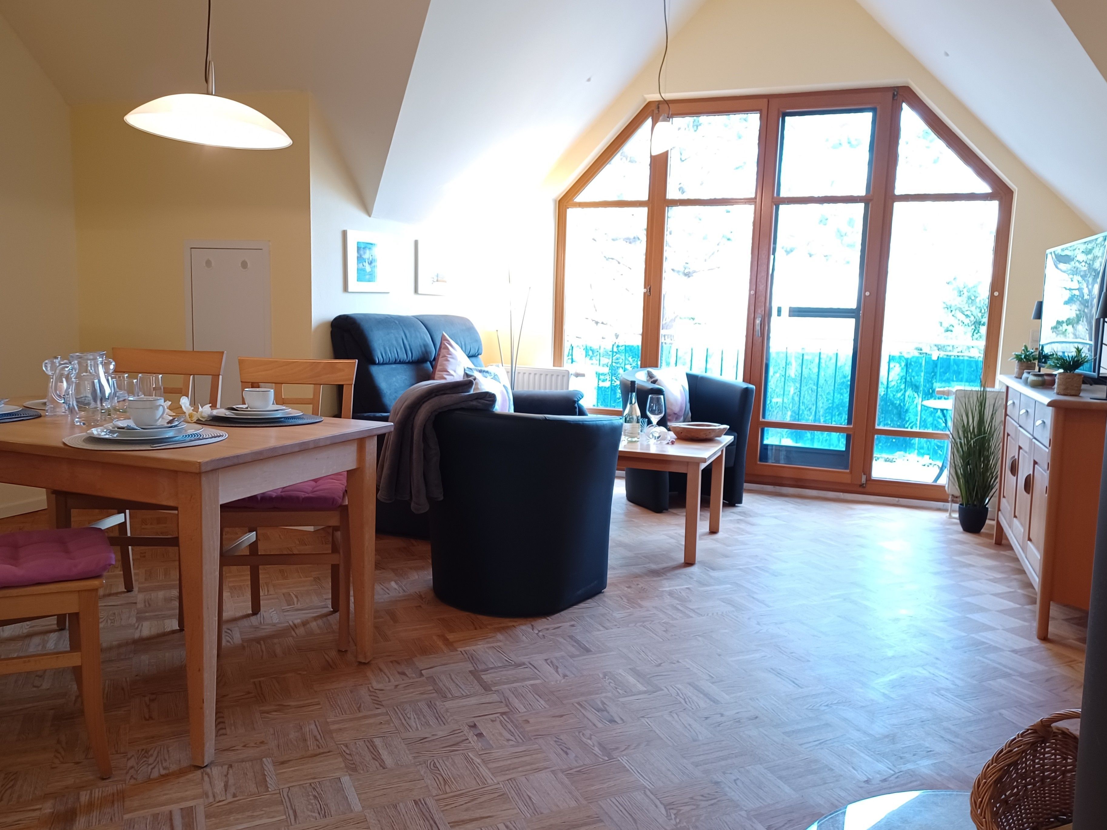 Ein Essbereich mit einem Holztisch, Stühlen und einem großen Fenster mit Blick ins Freie.