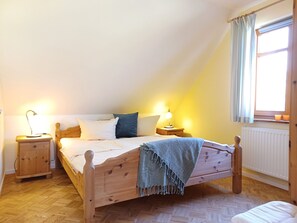 A bedroom with a wooden bed, two bedside tables, a window with curtains, and a radiator.