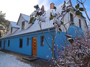 A two-story building with a blue exterior, a brown door, and a tiled roof covered in snow.